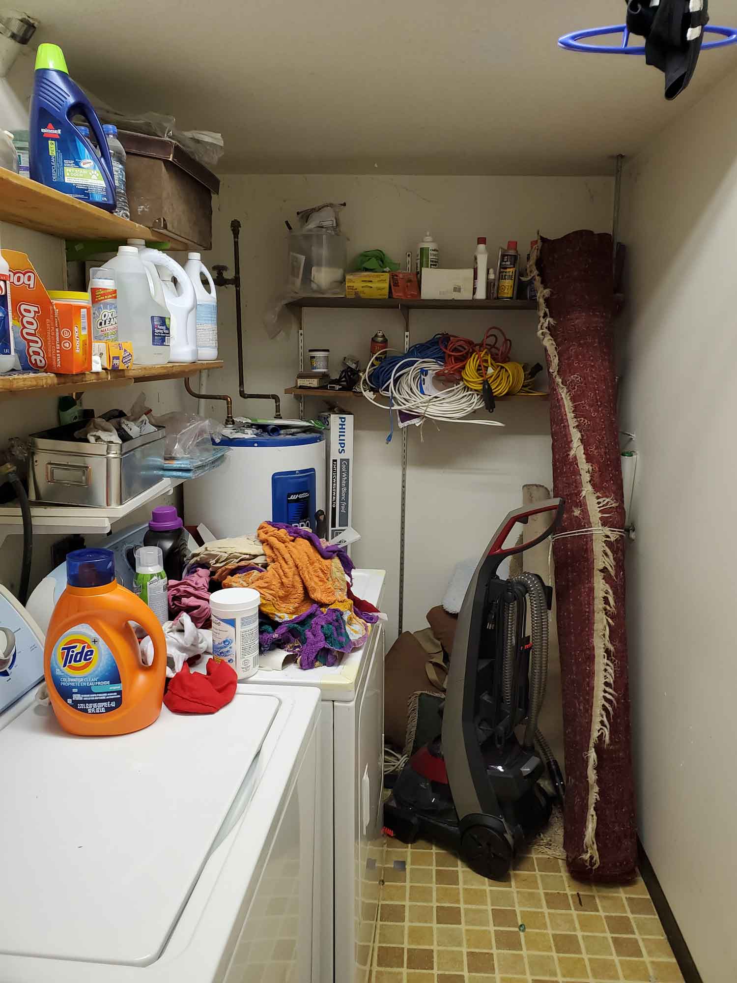 A laundry room with items taking up floor space and stacked on a side table and the dryer