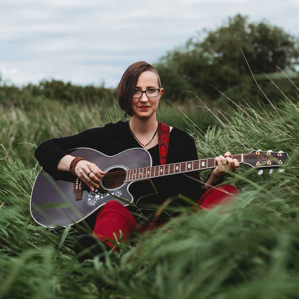 Jayne Karma Lamo sitting in a grassy field with a guitar